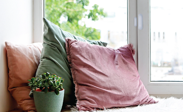 close up of contact sensor mounted on a window with bench and pillows below