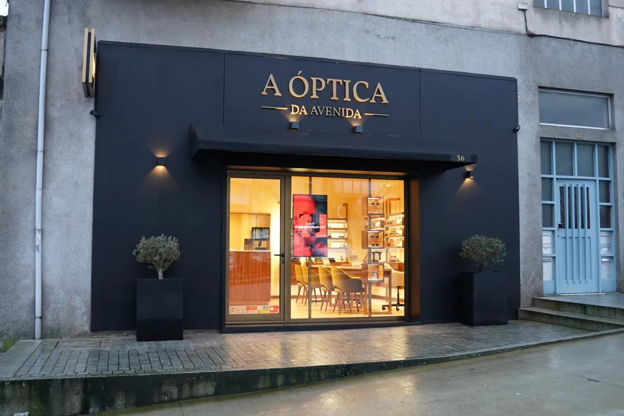 Fachada noturna da A Óptica da Avenida com letreiro dourado