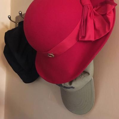 A red hat hangs over a golf cap on a rack.