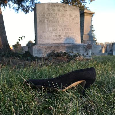 Black high heel on grass with gravestone in background