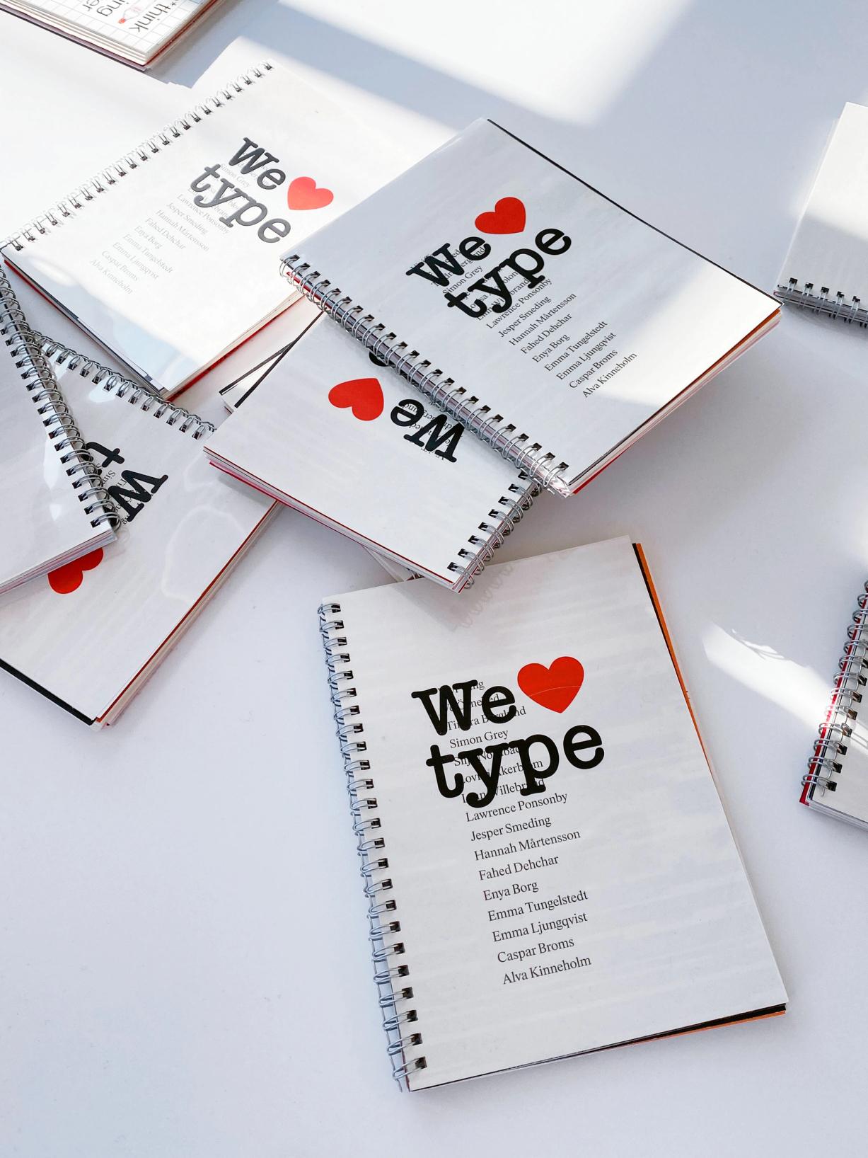 Spiralbundna häften med titeln "We ♥ type" och en lista med namn på omslaget, utspridda på ett vitt bord.