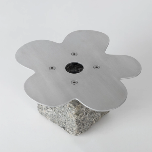 Blomformad metallplatta med ett hål i mitten, fastskruvad på ett granitblock, mot vit bakgrund.