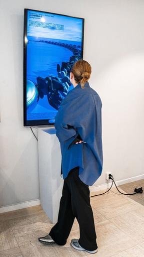 Besökare i blå skjorta står framför en stor stående skärm med en digital havsvy i utställningen.