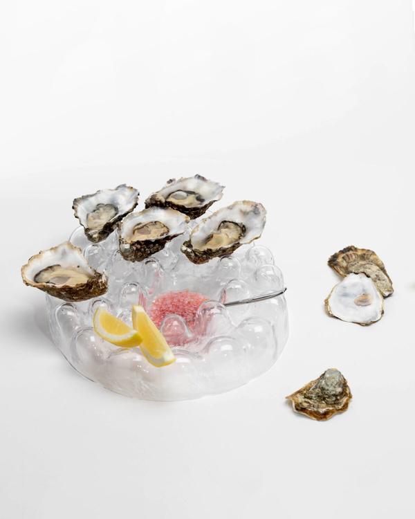 Serveringsfat i bubbligt klart glas med öppnade ostron, citronklyftor och en rosa sås i mitten, fler ostron bredvid.