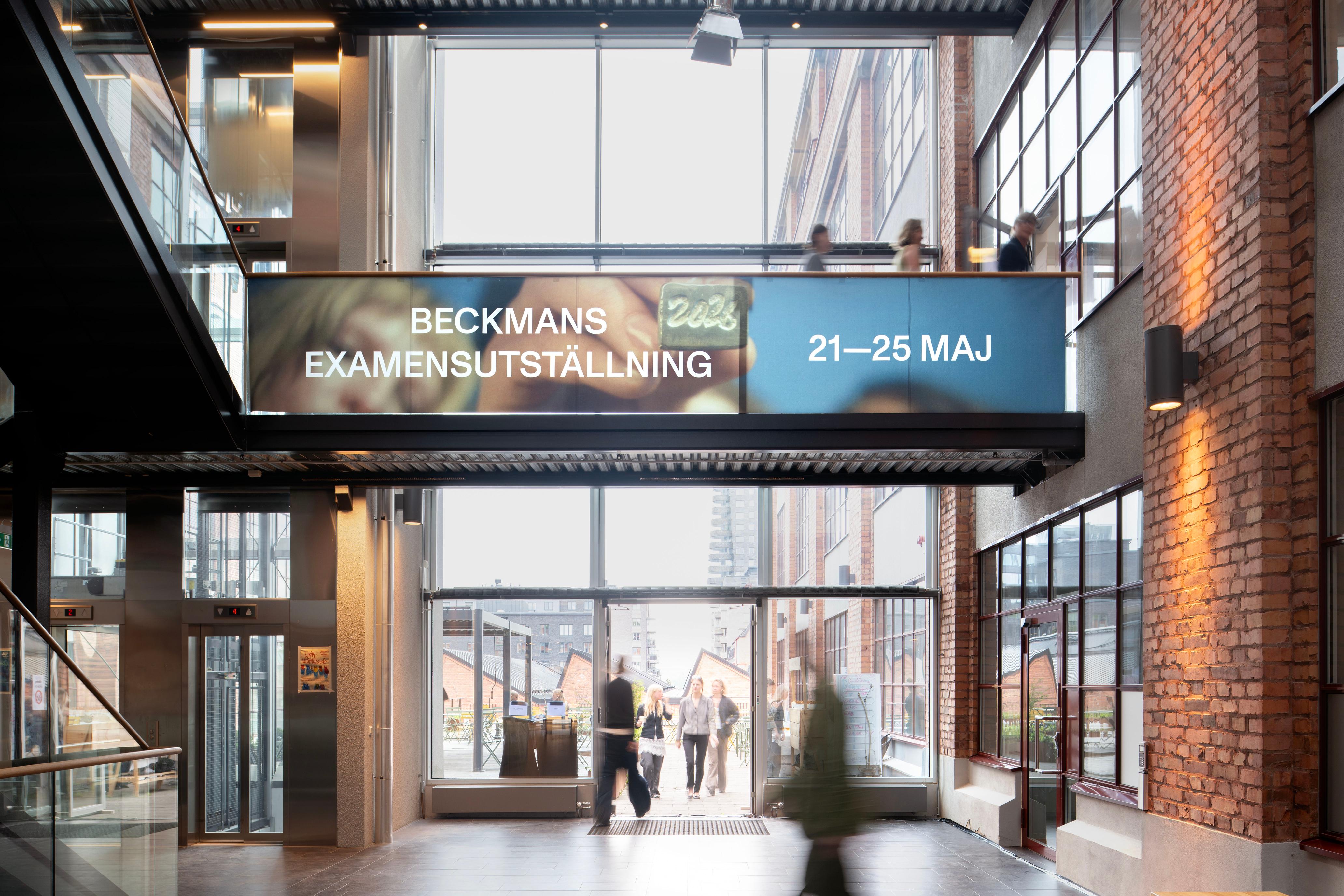 Banderoll för Beckmans examensutställning 21–25 maj på en gångbro i en ljus entréhall med tegelväggar, människor rör sig nedanför.