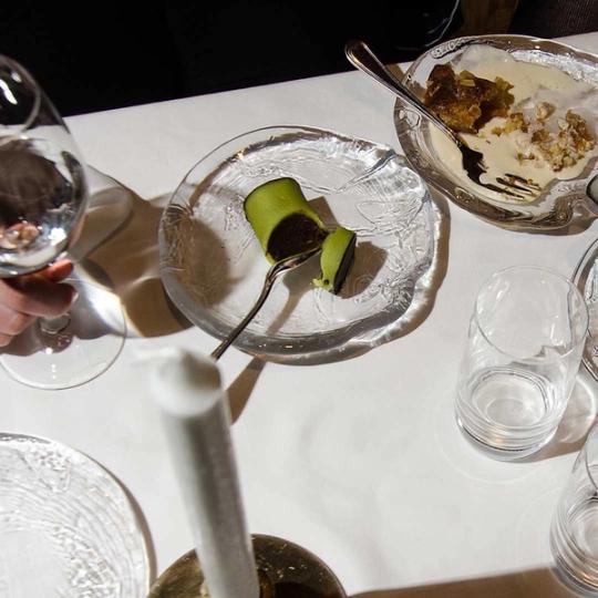 Dukat bord med strukturerade glastallrikar, en uppskuren punschrulle och en dessert i en skål, glas och ett vitt ljus.
