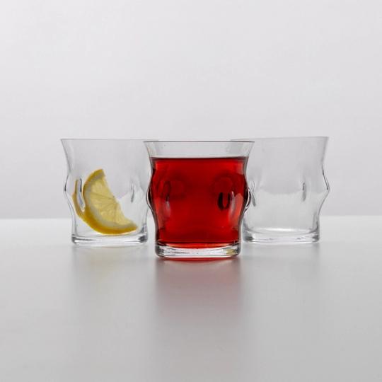Tre glas med intryckta gropar, ett med en citronskiva, ett med röd dryck och ett tomt, mot vit bakgrund.
