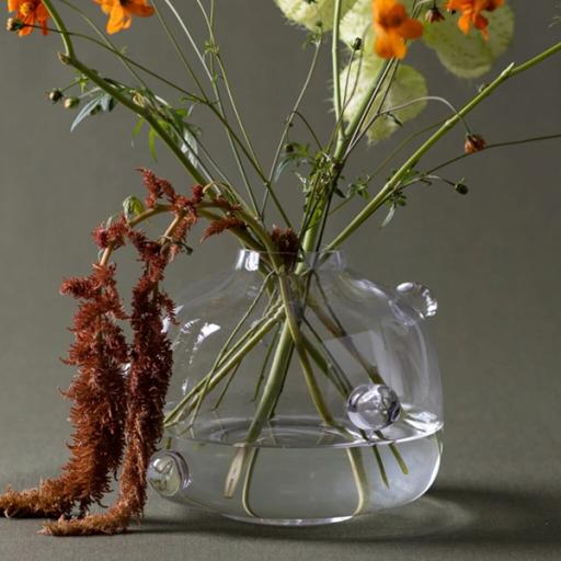 Rundad glasvas med små glaskulor på sidorna, fylld med orange blommor, gröna stjälkar och hängande rostfärgad amarant.