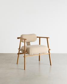 Fåtölj med stomme av runda träribbor och rundade beige klädda sits- och ryggdynor, på betonggolv.