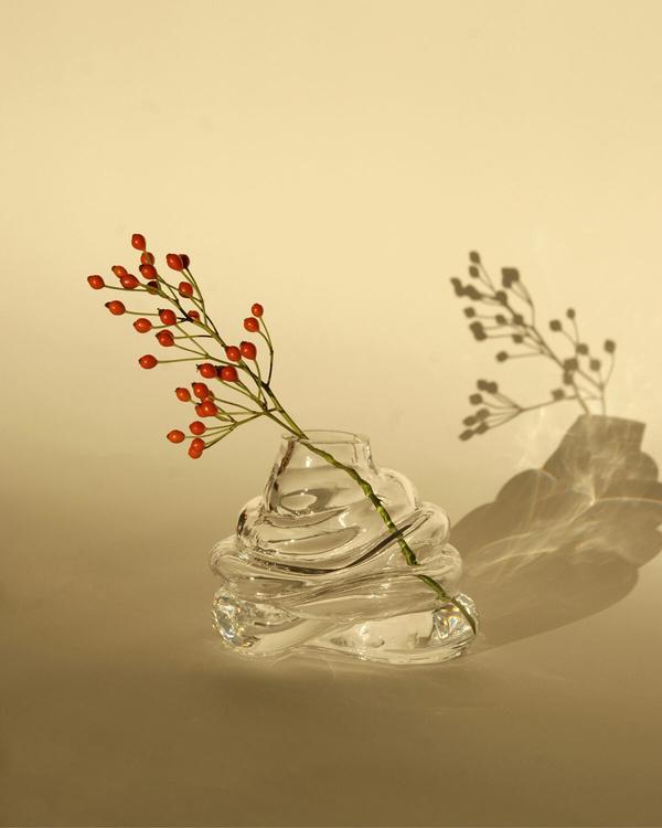 Liten vågformad glasvas med en kvist röda bär, som kastar skugga mot en beige bakgrund.