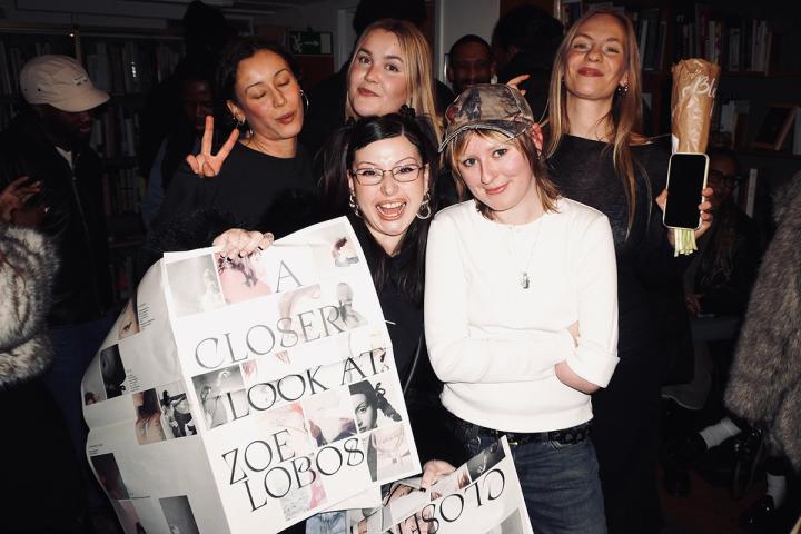 Glada människor poserar på en vernissage, en håller upp en uppslagen tidning med foton.