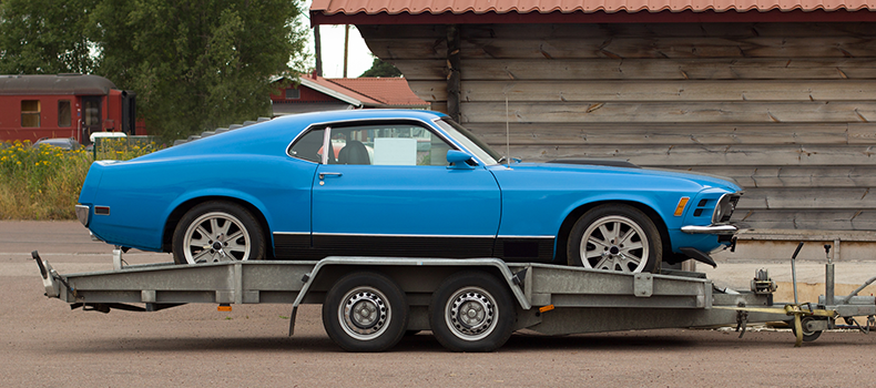 a blue non-running vehicle loaded on an open trailer for transport
