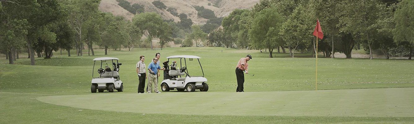 man in red shirt and black pants on golf course with two golf carts behind him