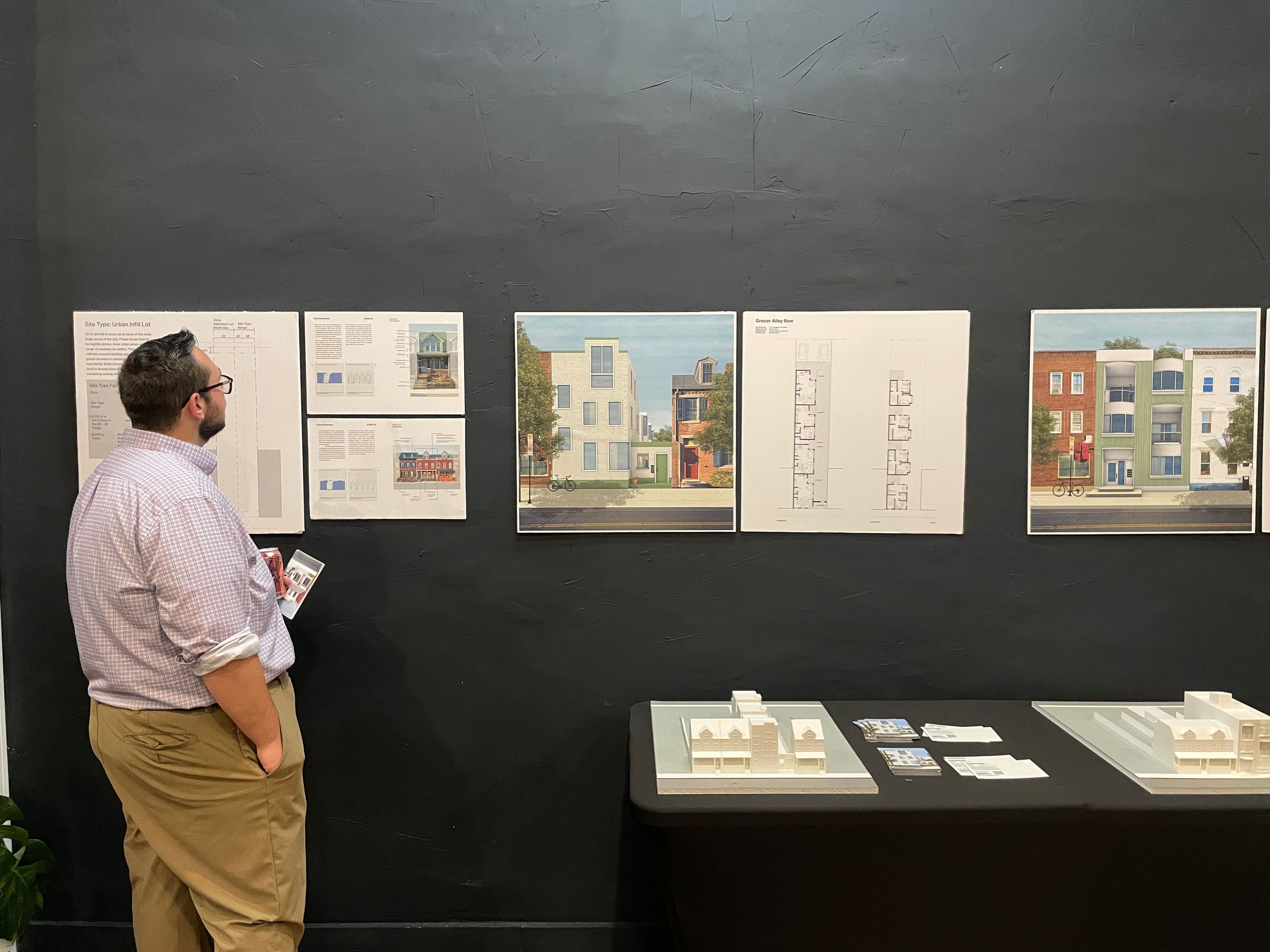 A man with his back to the camera looks at renderings on a wall.