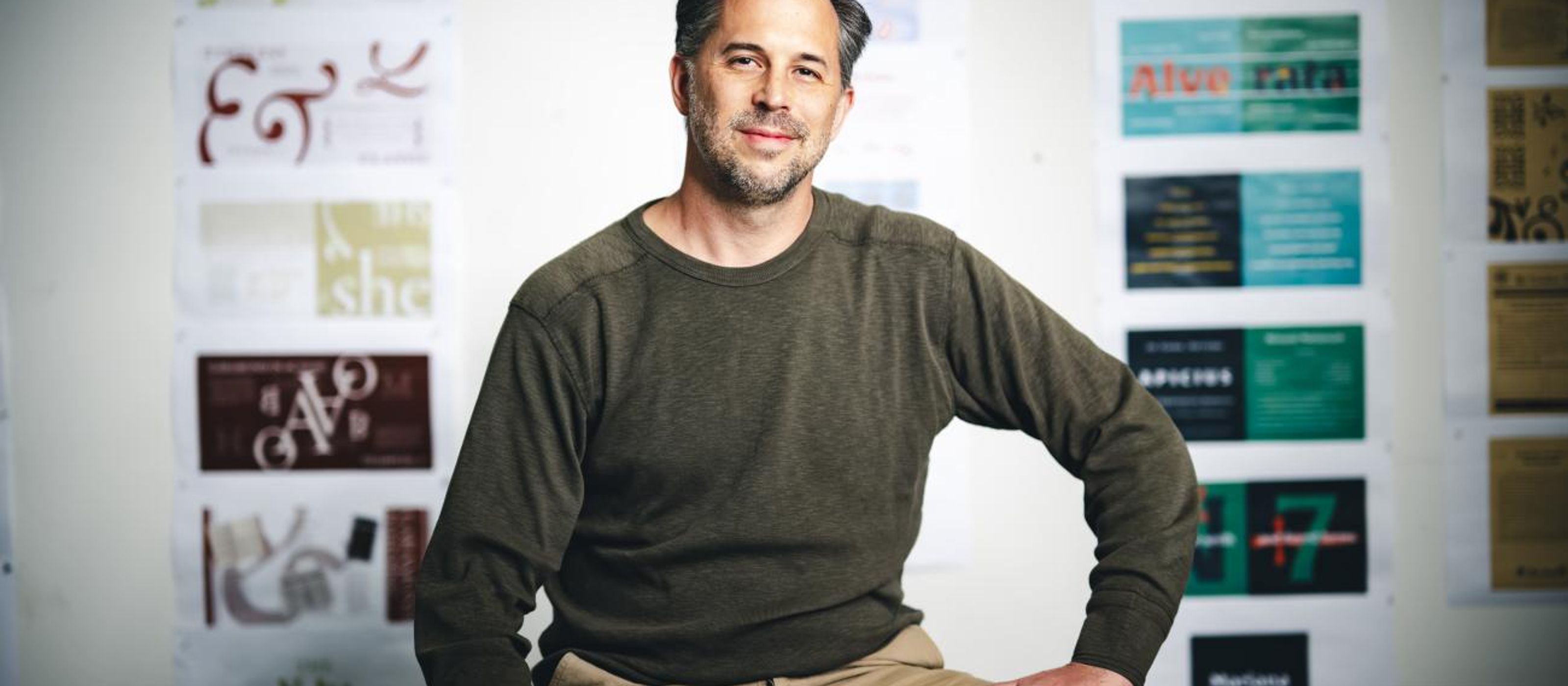 Kevin Lahoda sits near a table with draft designs on a board behind him.