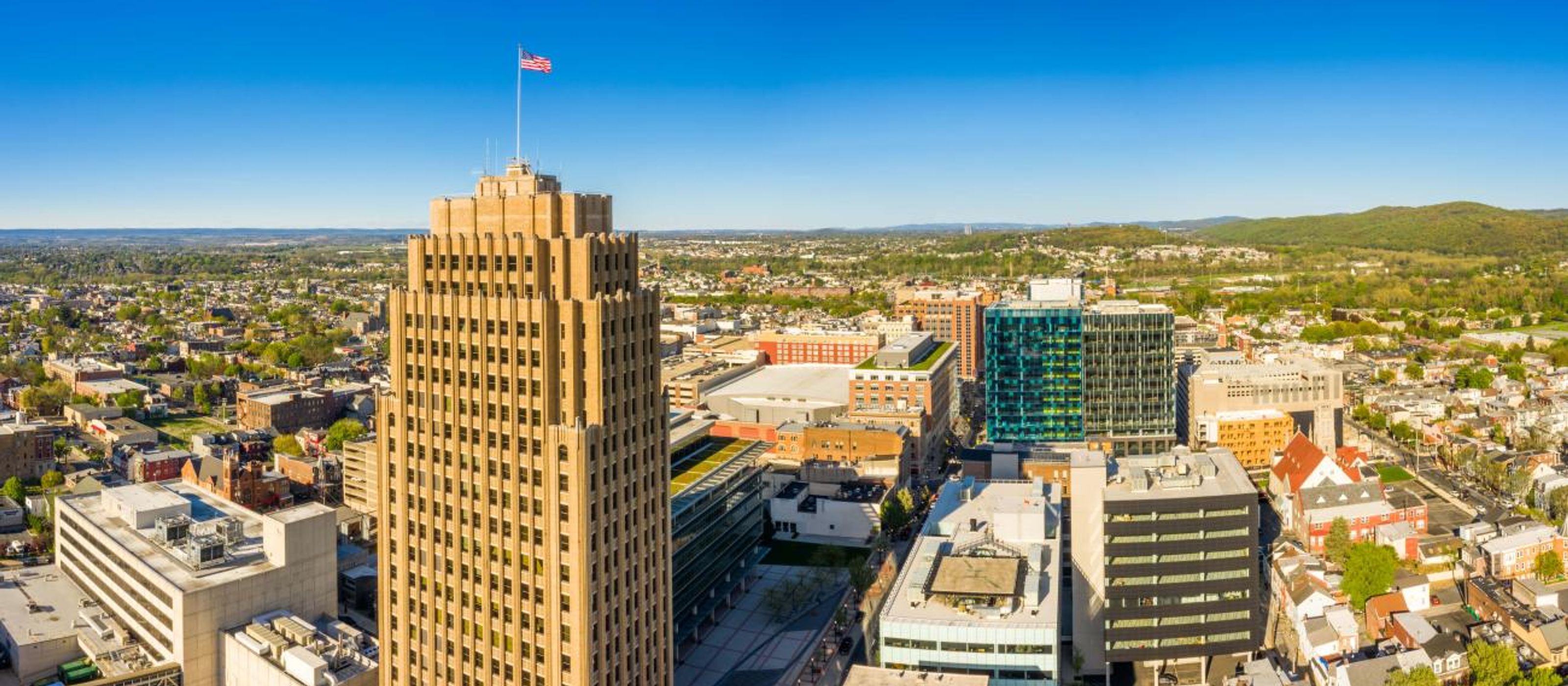 A view of Allentown city scape from above with a clear blue sky and green trees on the horizon.