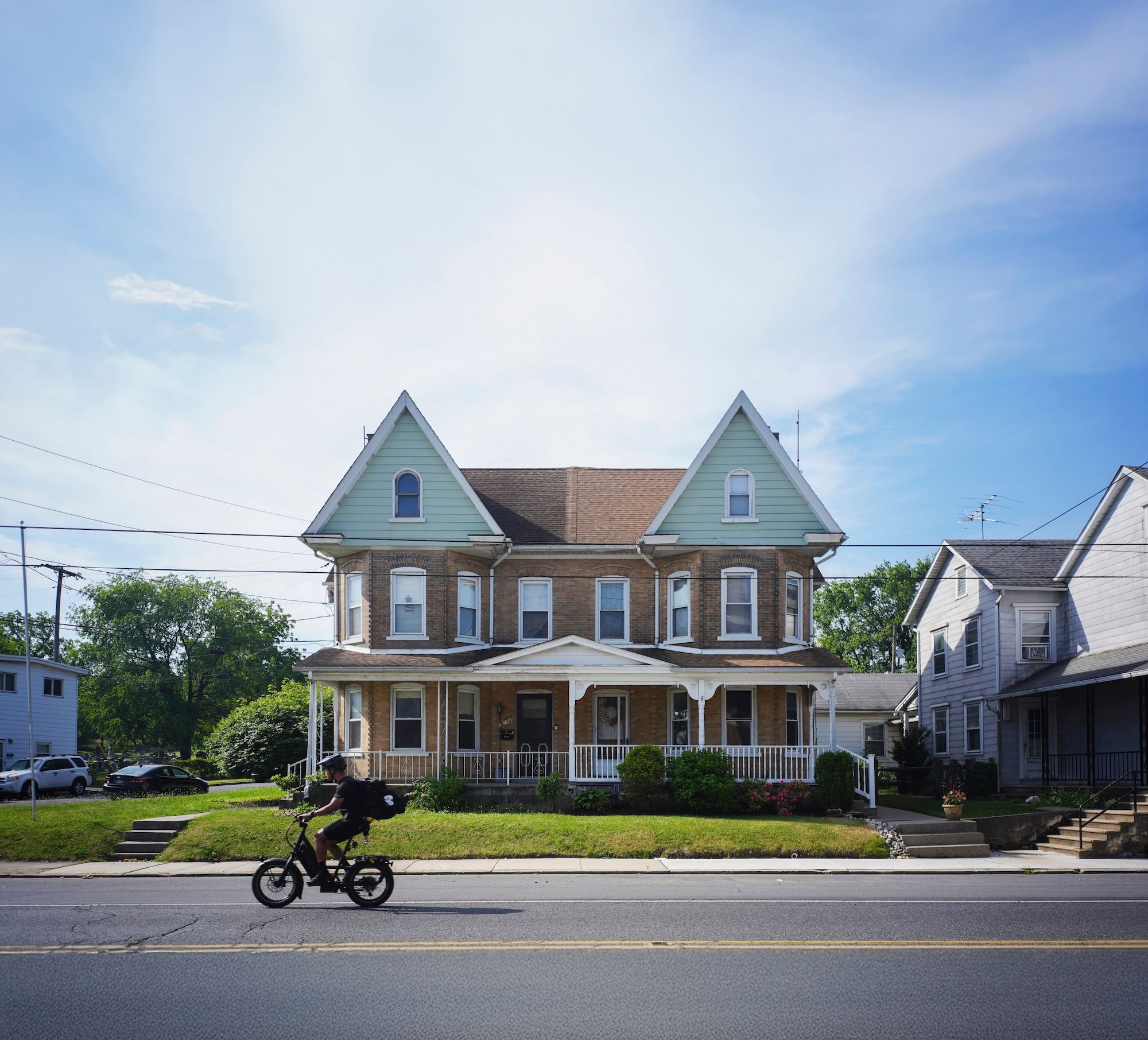 A twin house in Allentown. Someone rides a motorbike on the street in front of the house.