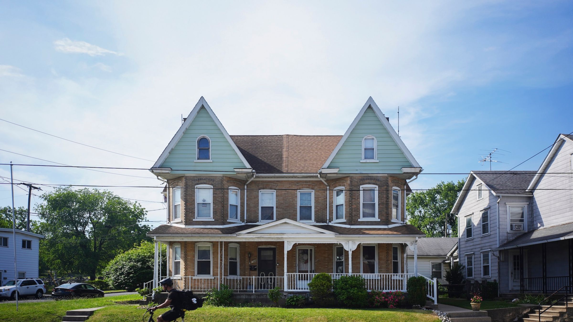 A twin house in Allentown. Someone rides a motorbike on the street in front of the house.