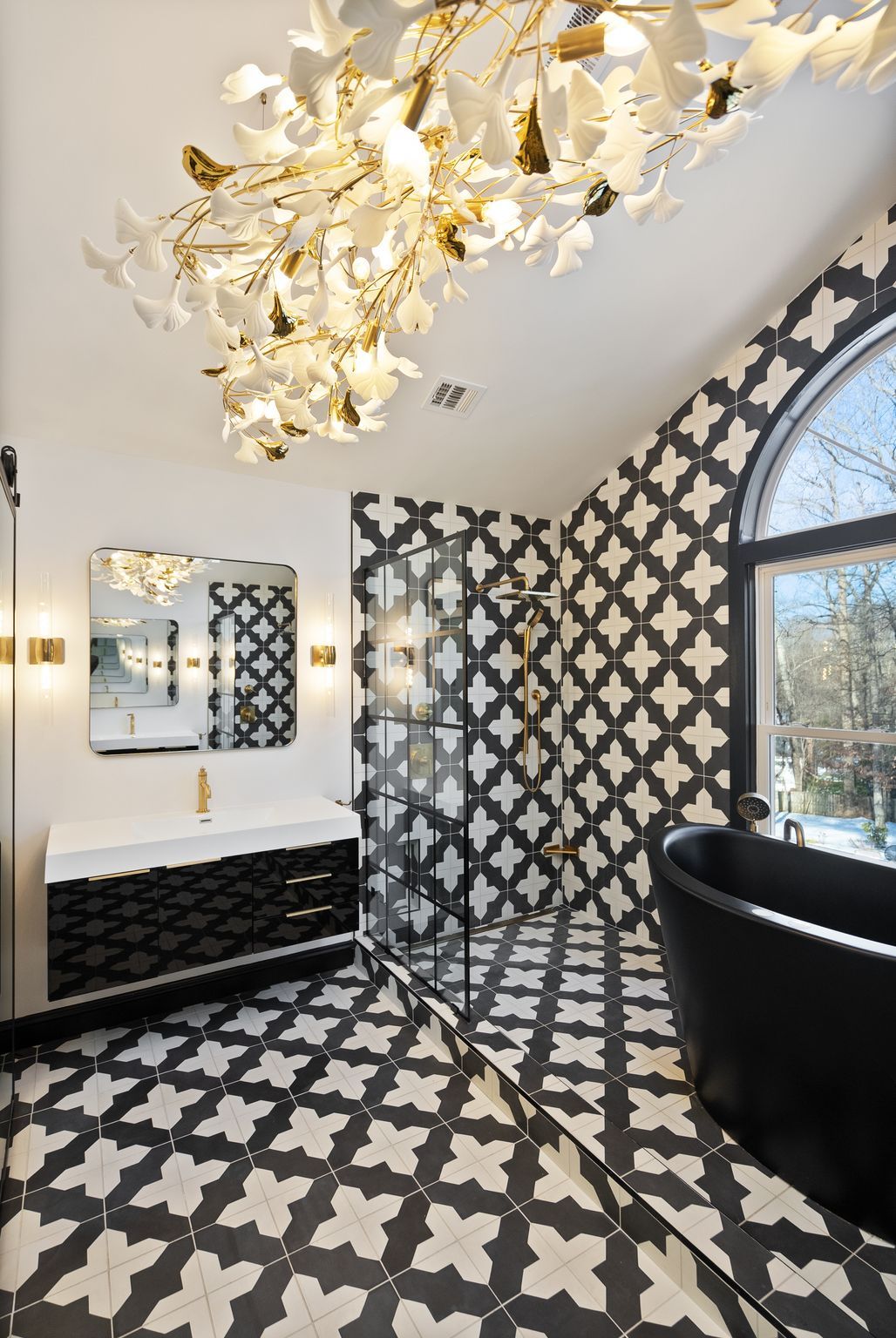 Spacious master bath with black and white patterned tiles, glass shower, and elegant chandelier.