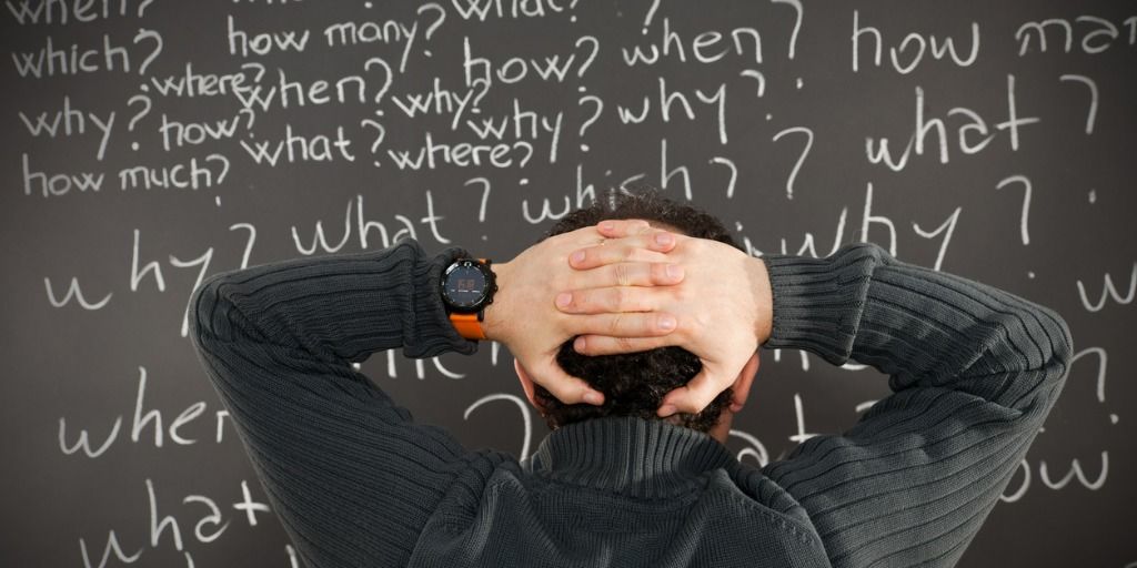 man confused by many question written on a blackboard