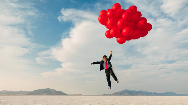 Boy in a business suit carried away by big red balloons