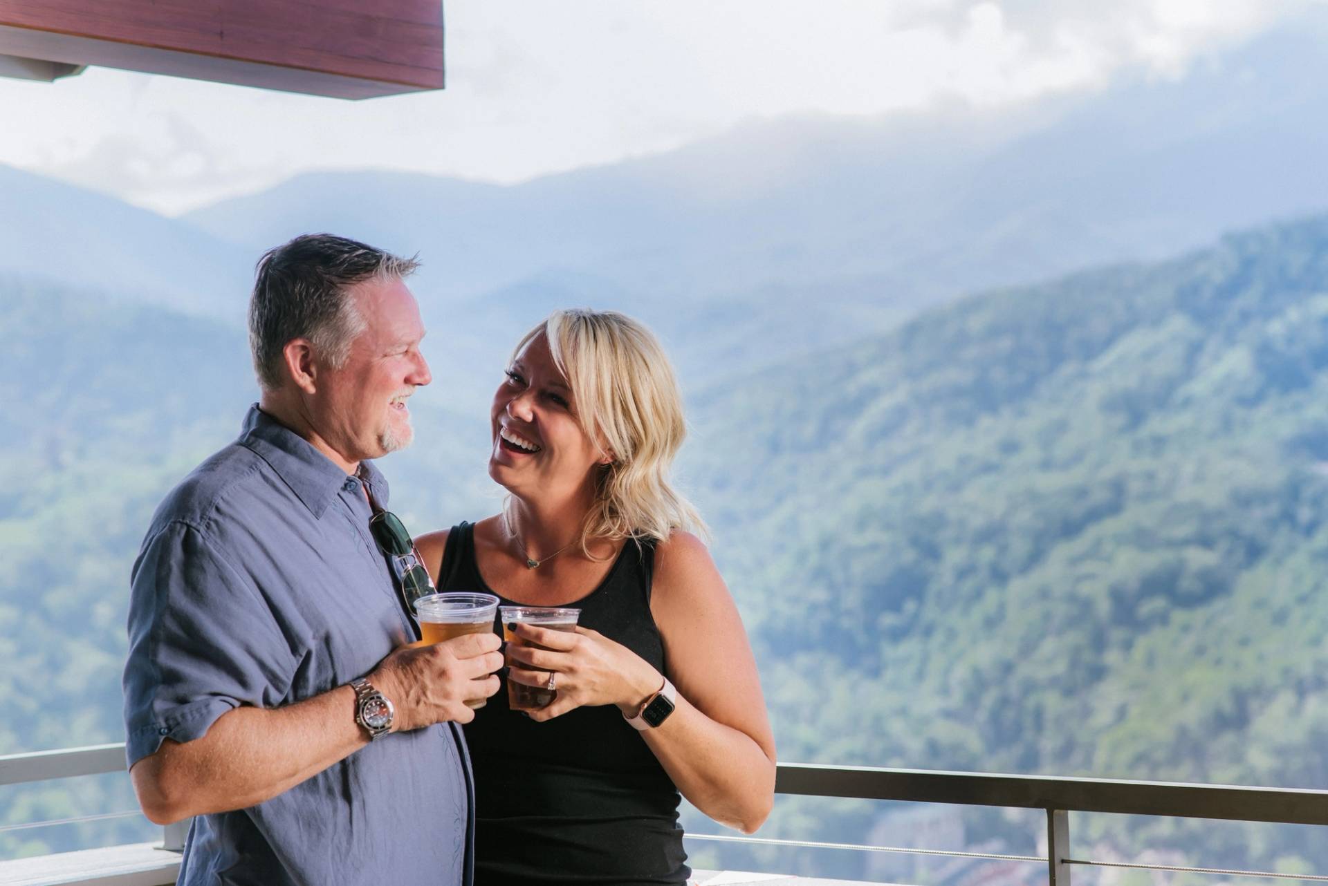 a couple smiles at each other as they enjoy their beers and take in the views from the SkyCenter