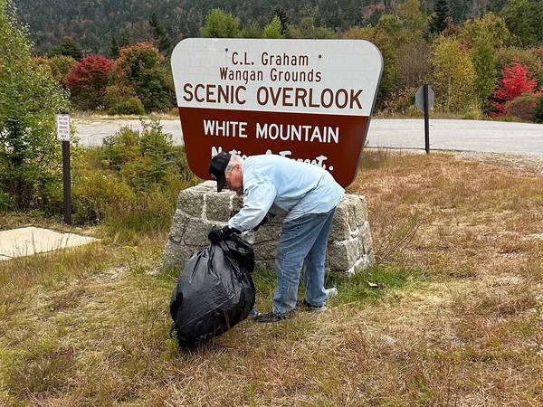 Loon team member picking up trash by a Kancamagus Highway Scenic Overlook sign.