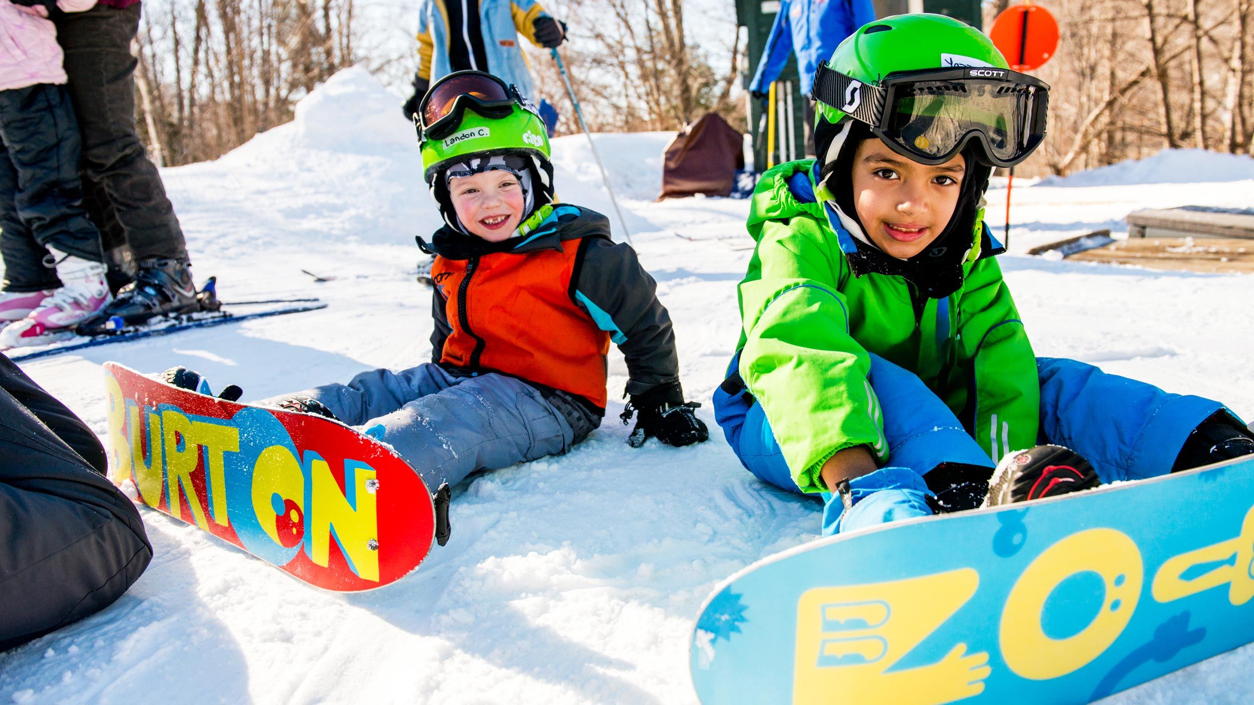 two little kids sitting on snow with their snowboards on