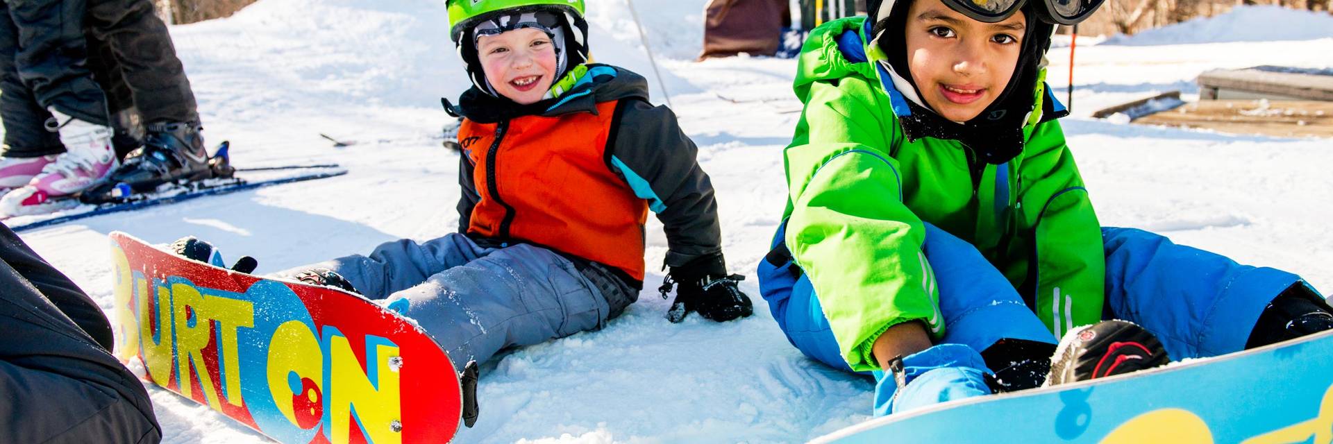 two little kids sitting on snow with their snowboards on