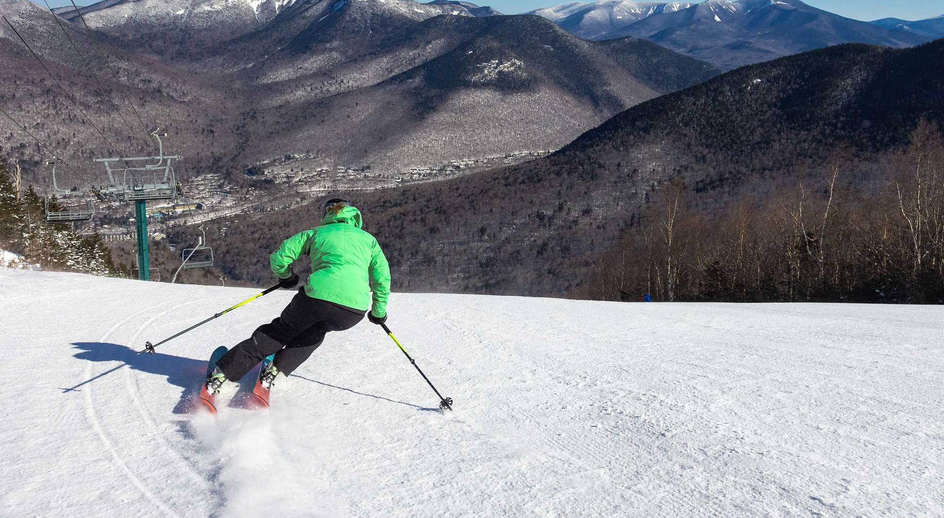 Woman in green jacket skiing away from the camera on Loon North Peak
