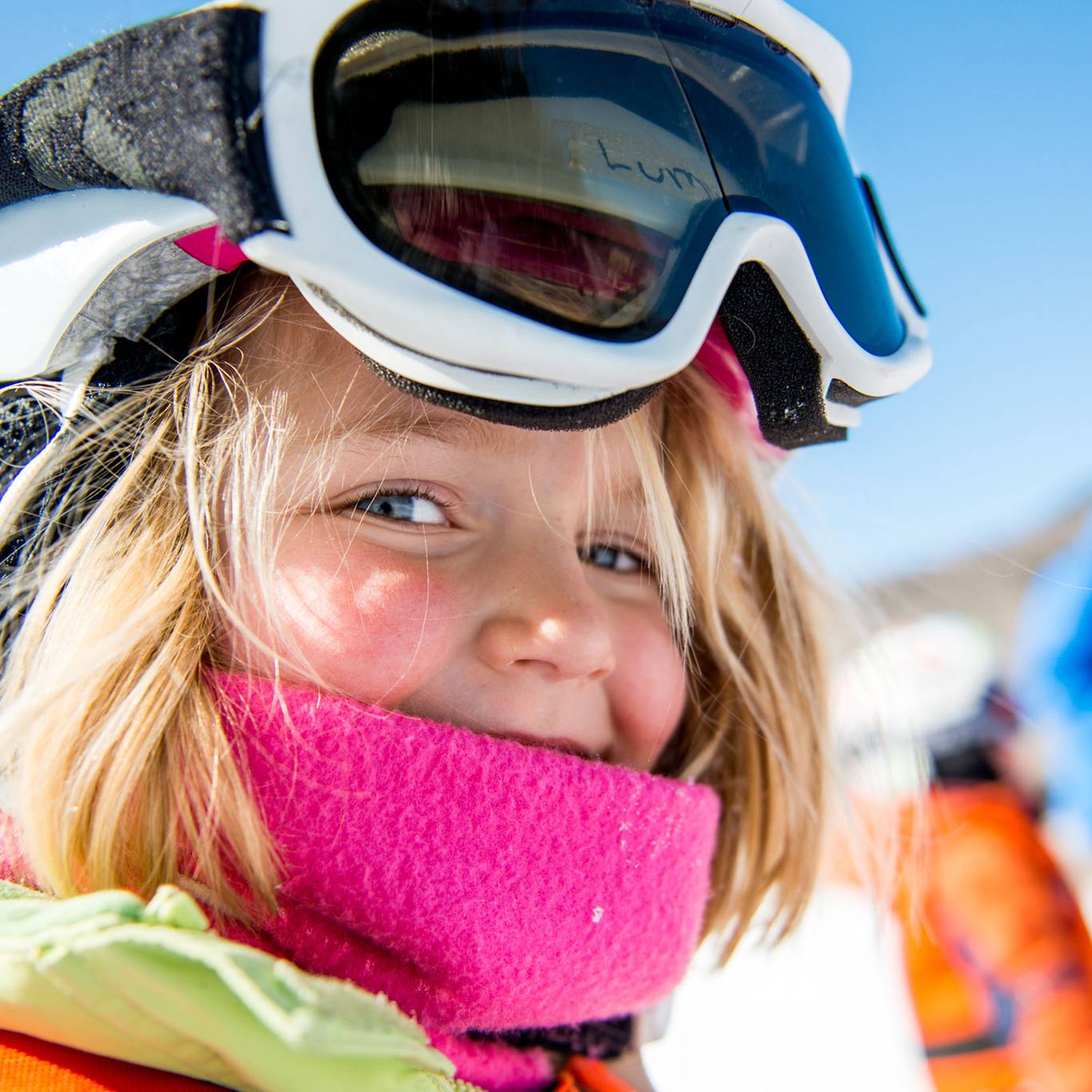 young girl wearing pink buff and helmet. Smiling at camera
