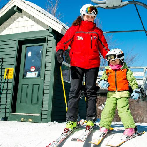 little skier getting off a chairlift with a coach