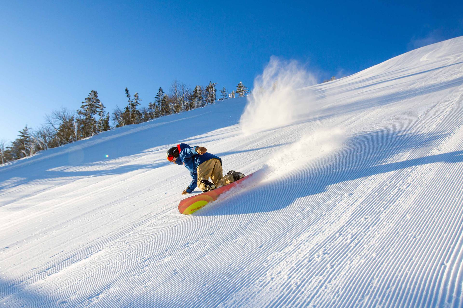 Snowboarder carving down fresh corduroy.
