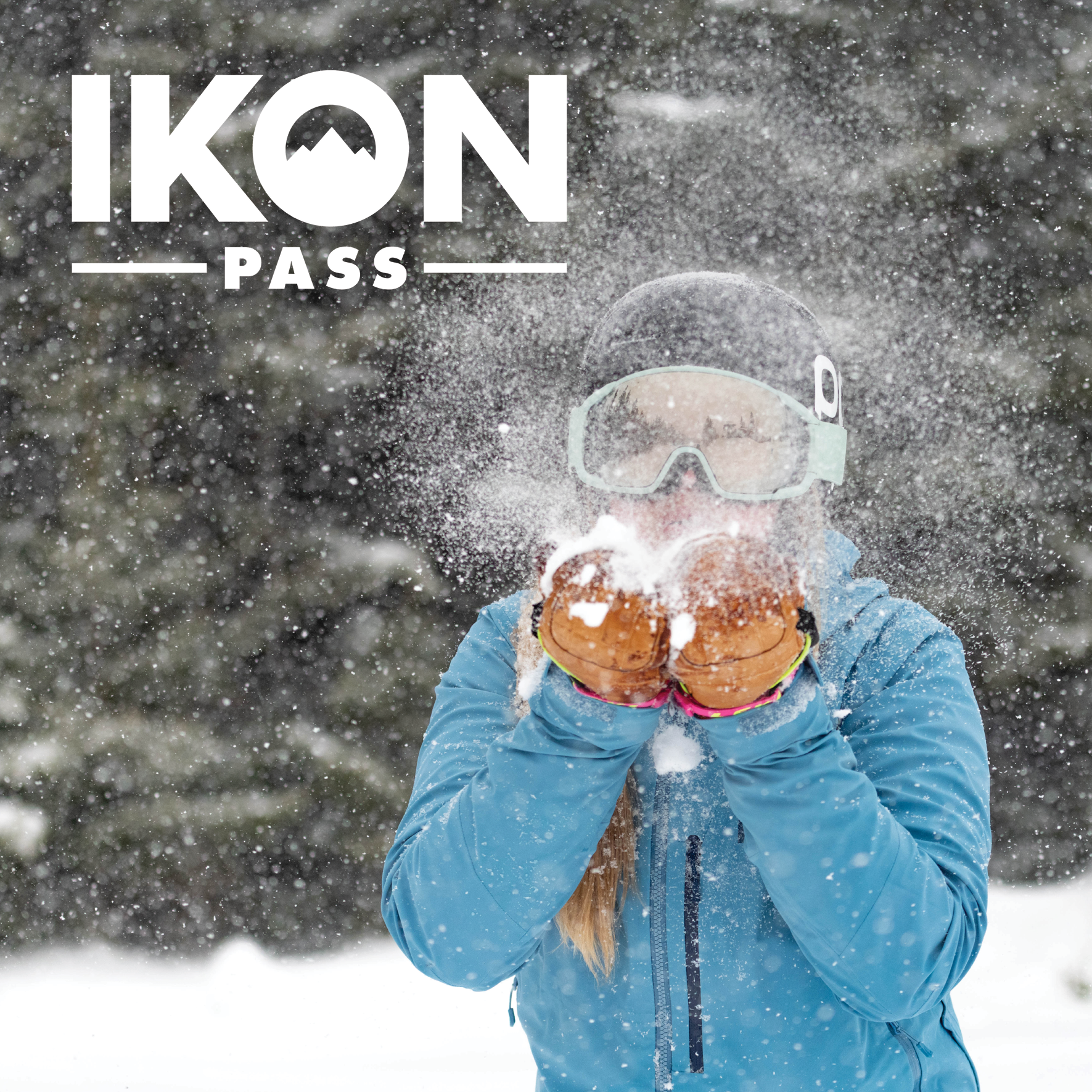 A skier blowing snow with the Ikon Pass logo