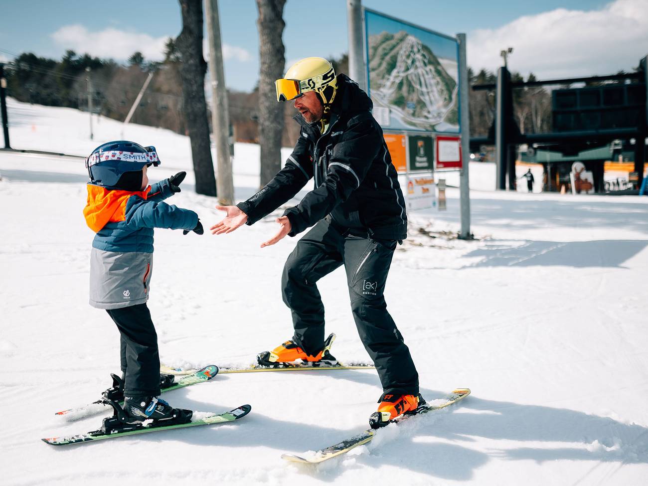 Instructor holds hands out while child skis toward him