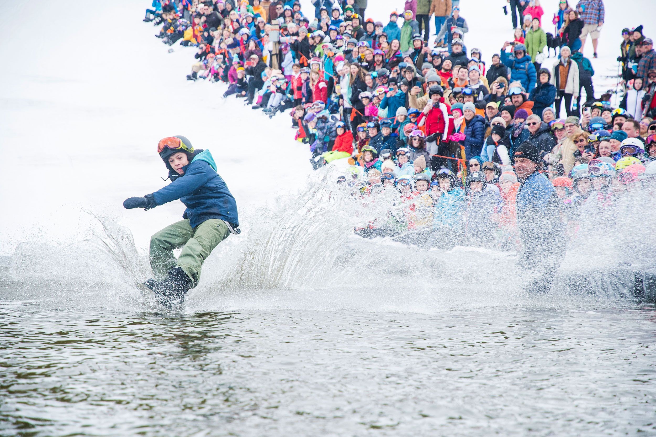 Snowboarder glides across the water in pond skim.