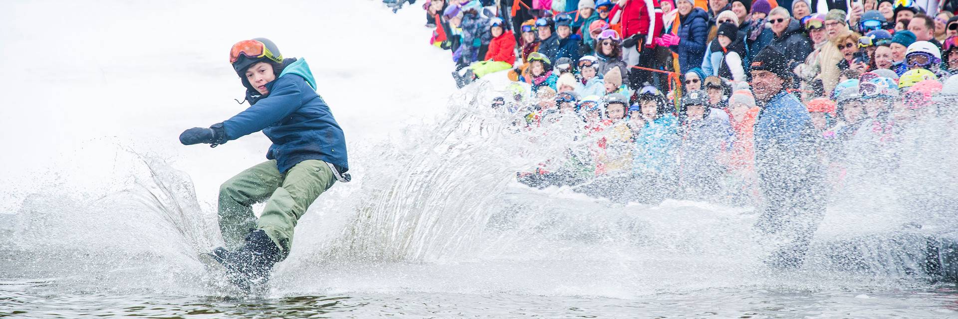 Snowboarder glides across the water in pond skim.