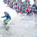 Snowboarder glides across the water in pond skim.