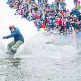 Snowboarder glides across the water in pond skim.