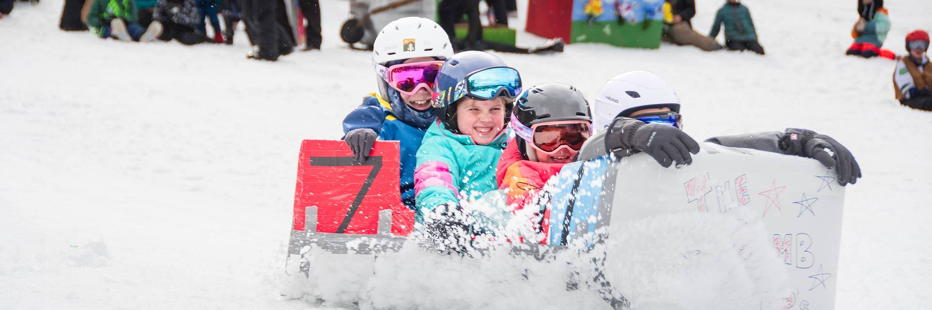 Four contestants sail down the snow in a carboard race cart
