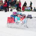 Four contestants sail down the snow in a carboard race cart