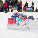 Four contestants sail down the snow in a carboard race cart