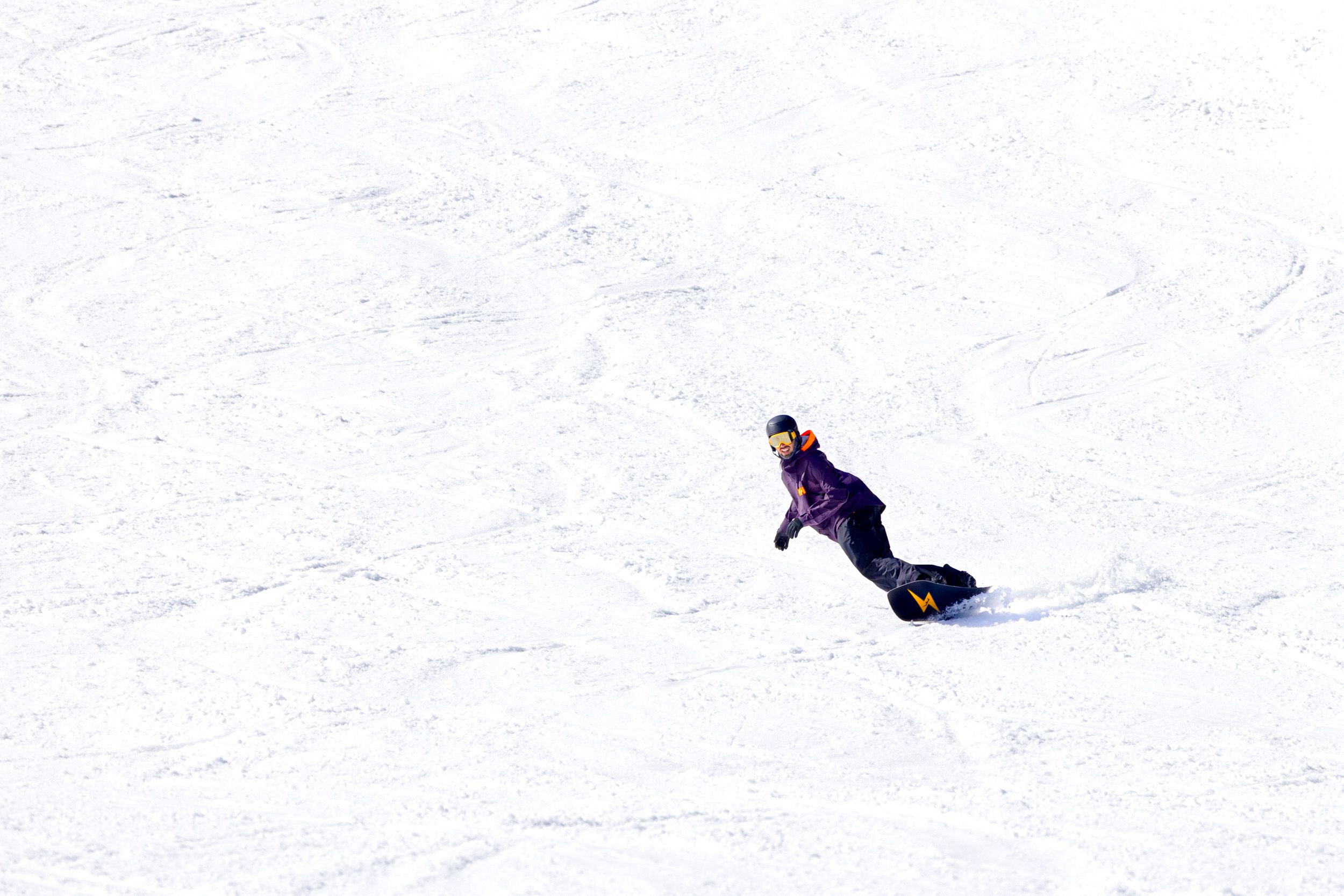 A snowboarder carves in corn snow