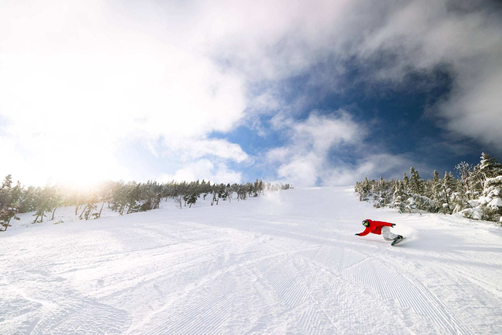 Snowboarder in red carves through perfect corduroy