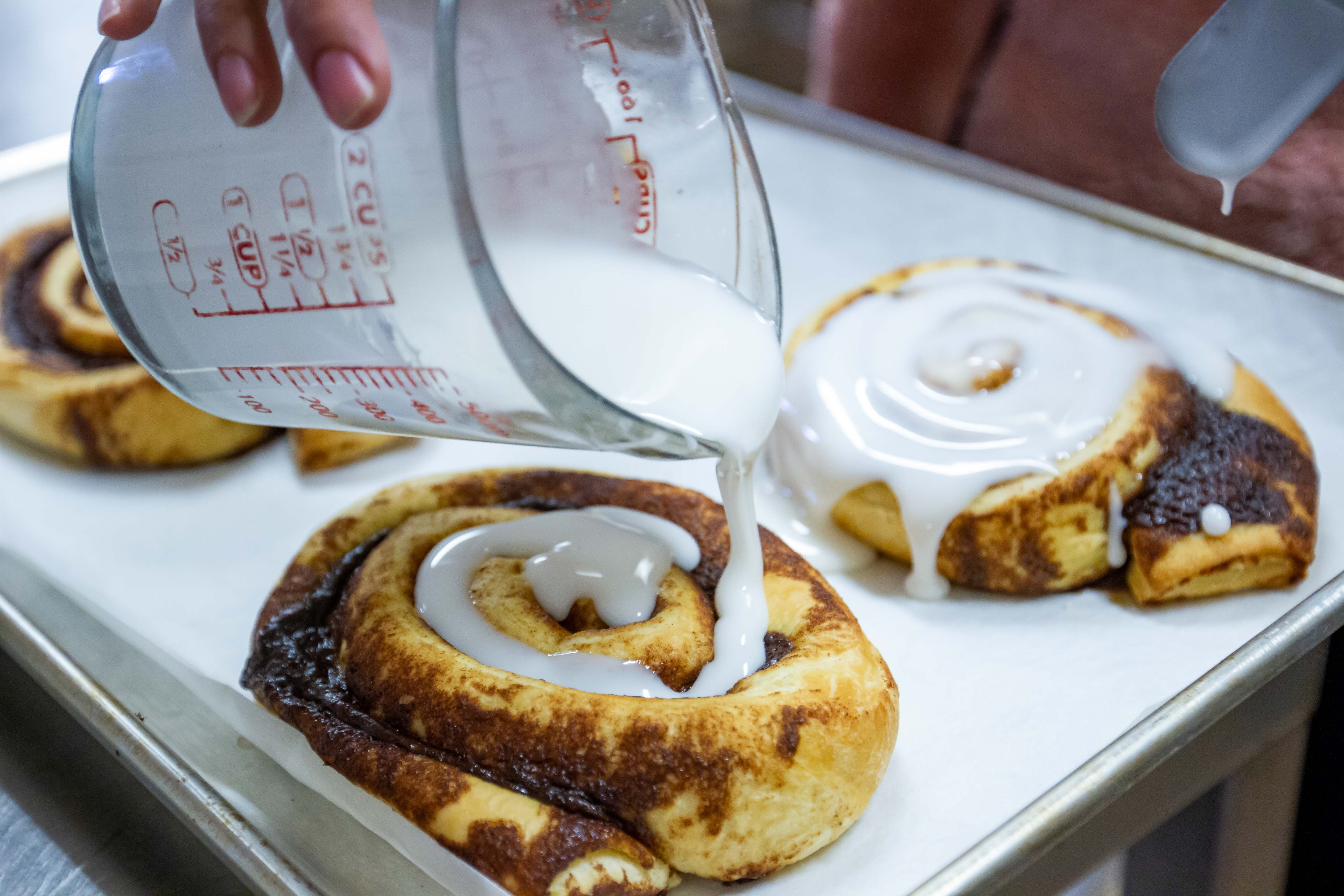 Chef pouring sweet, ooey gooey glaze on fresh cinnamon rolls 