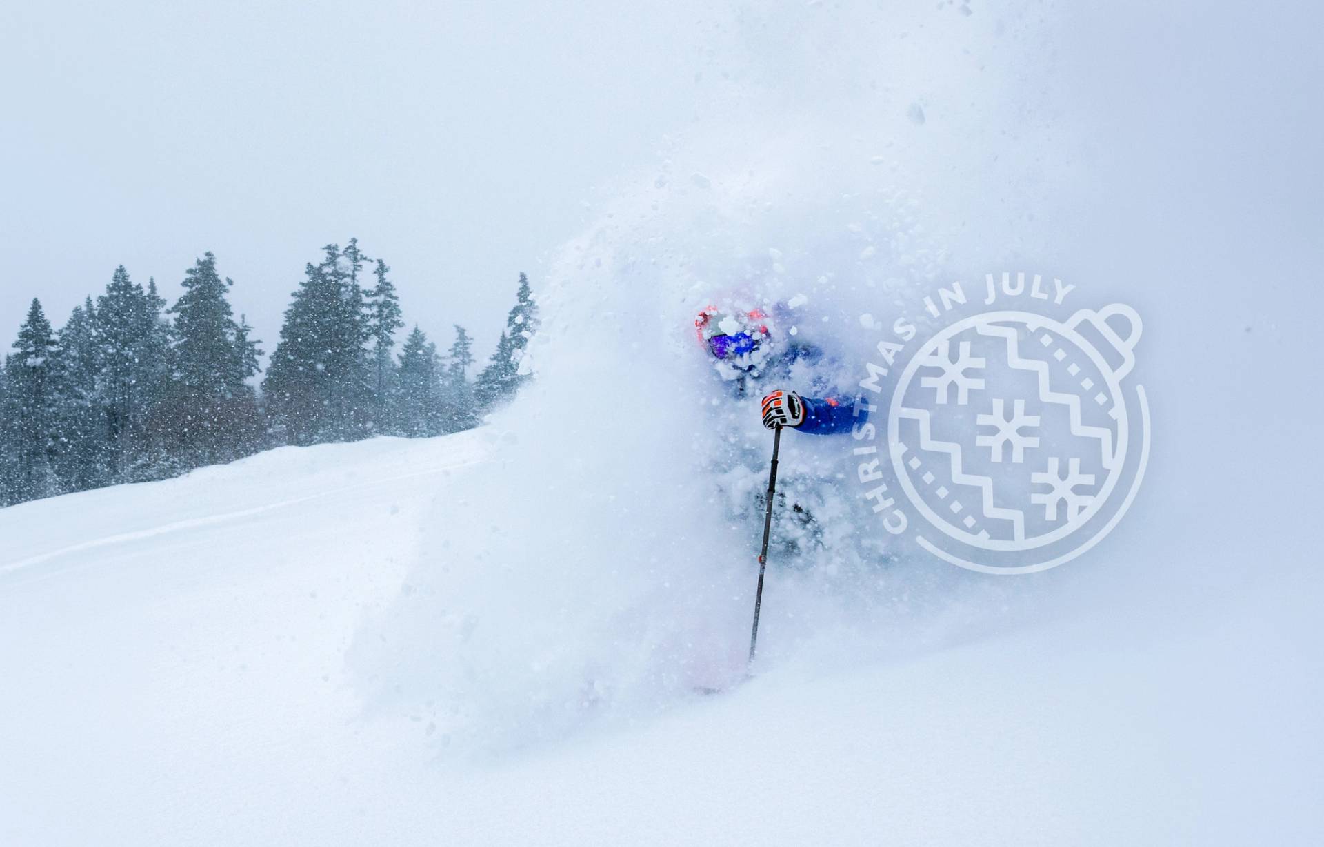 Skier in purple makes a powder turn on Hayburner with  a Christmas in July logo transparent over the shot