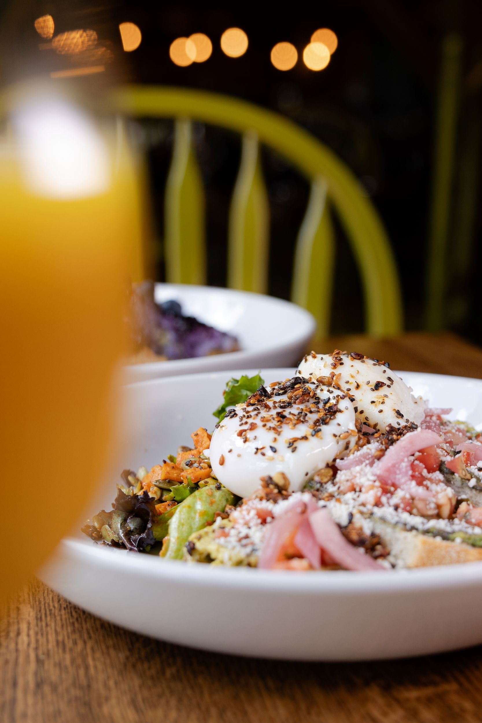 Two bowls of fresh food with a wine glass in view