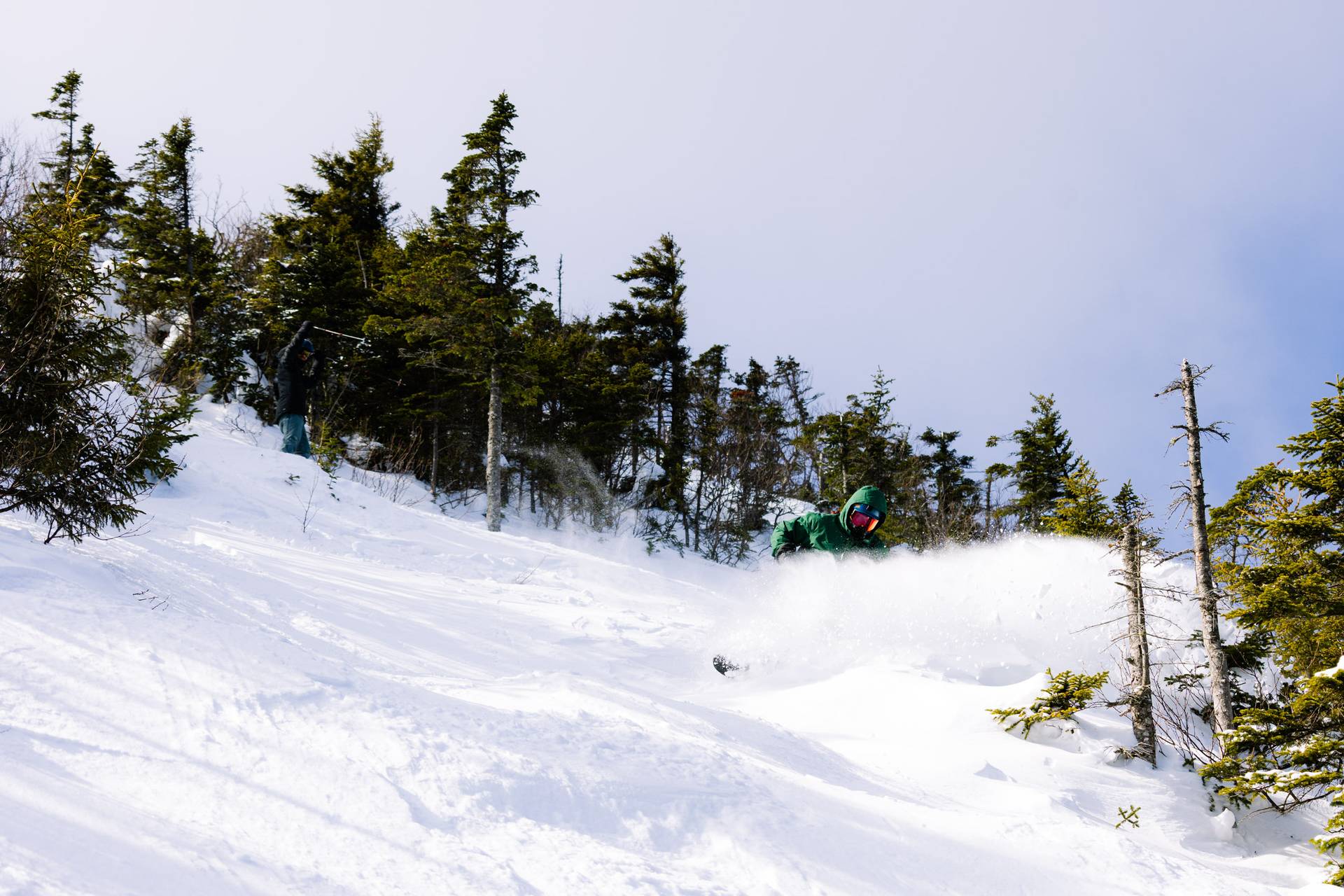Snowboarder in green finds a powder stash off of Spillway Crosscut