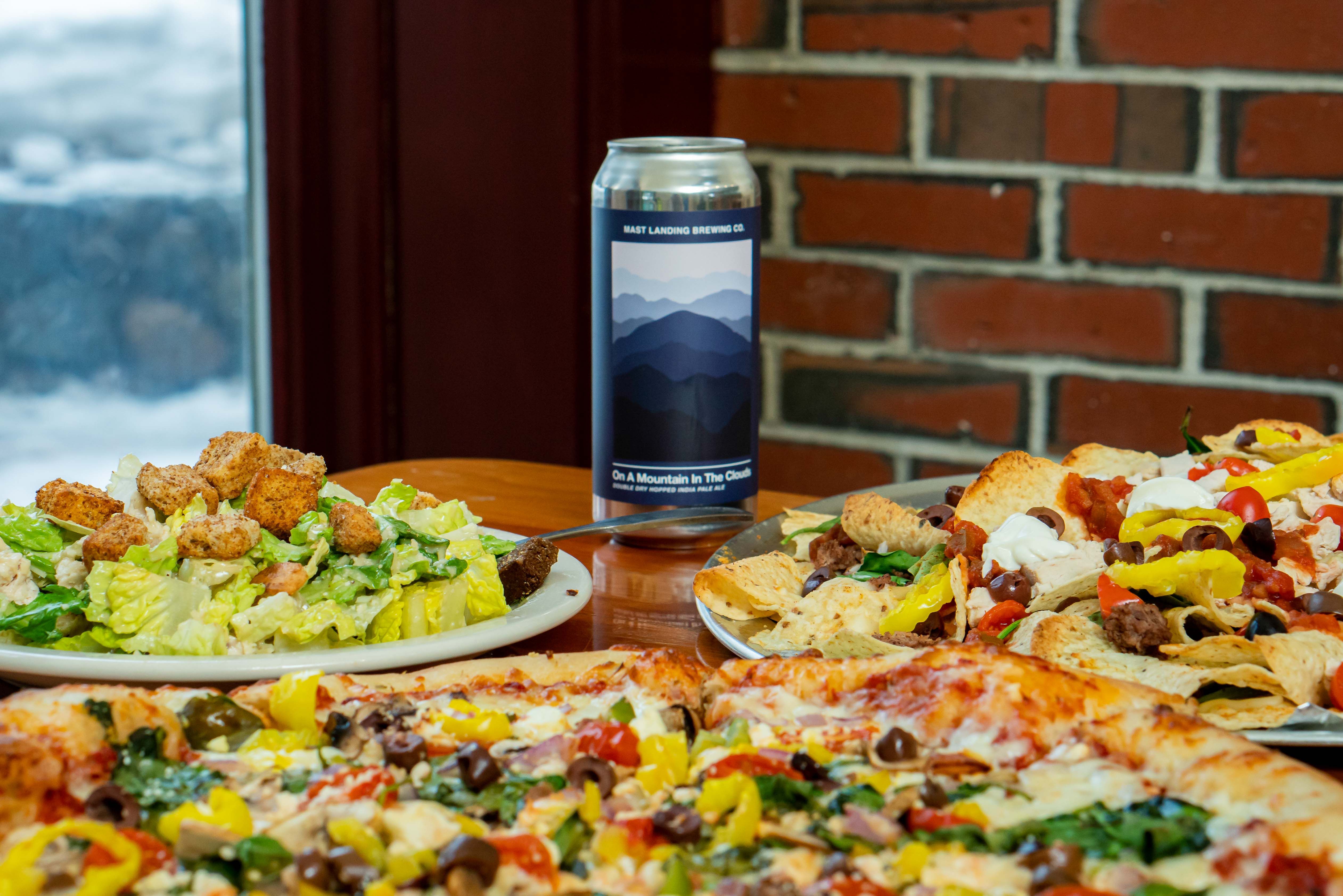 Pizza, nachos, and a salad on a table with a beer can