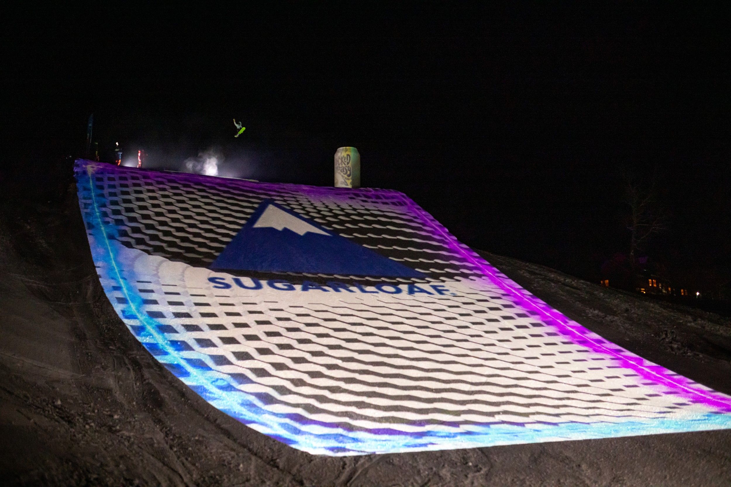 Snowboarder at the top of a large illuminated jump
